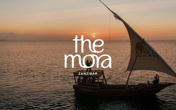 Kleines exotisches Segelschiff vor Sonnenuntergang und Logo von the mora zanzibar